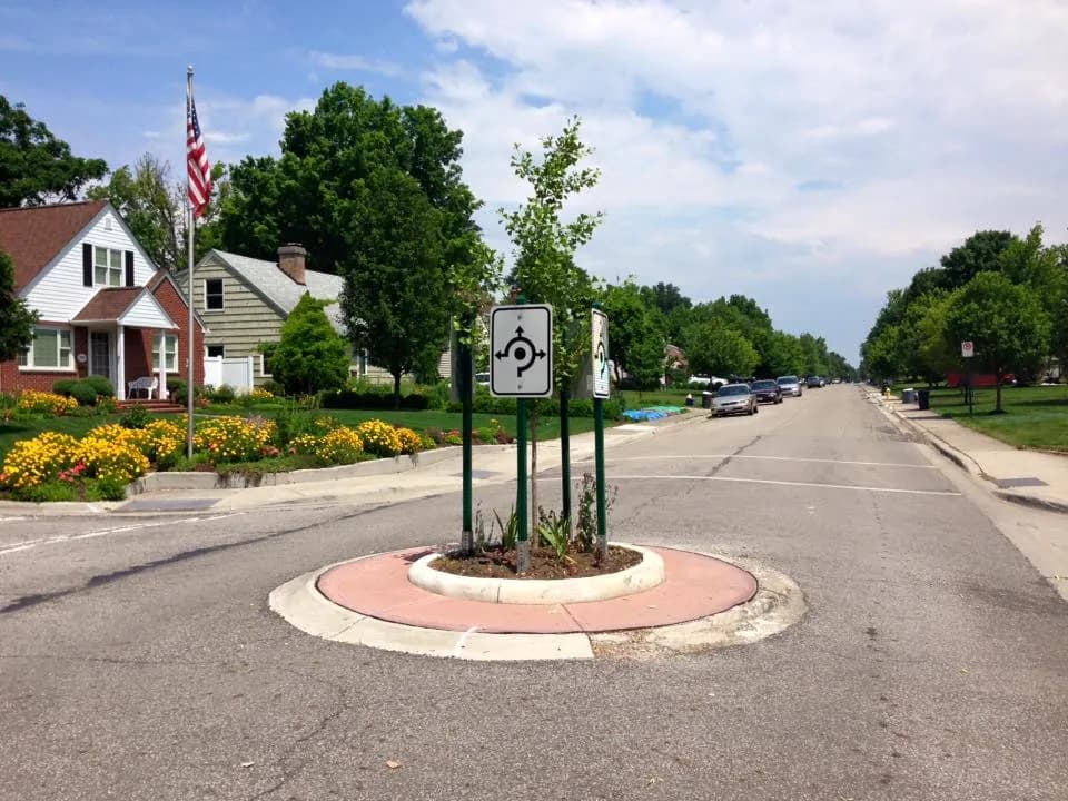 A small landscaped roundabout on a residential Upper Arlington street with an American flag